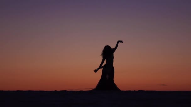 Dançarina segura um véu em suas mãos, ela dança uma dança do ventre na praia. Silhueta — Vídeo de Stock