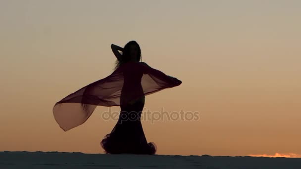 Menina na praia dança graciosamente seu corpo contra o pôr do sol. Silhueta — Vídeo de Stock