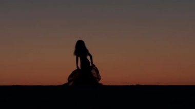 Kız incelikle eller bir günbatımı karşı bir örtü ile dans ediyor. Siluet