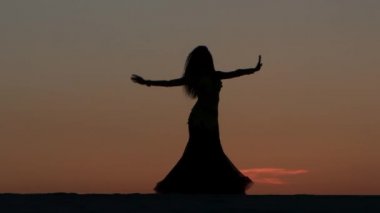 Kız oryantal güzel gün batımını karşı sahilde dans dans ediyor. Siluetleri