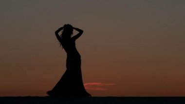 Kız oryantal güzel gün batımını karşı sahilde dans dans ediyor. Siluetleri