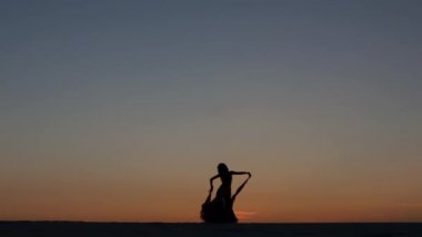 Kız oryantal güzel gün batımını karşı sahilde dans dans ediyor. Siluetleri