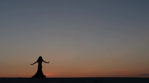 Menina dançando barriga dançando na praia contra o pôr do sol. Silhuetas — Vídeo de Stock
