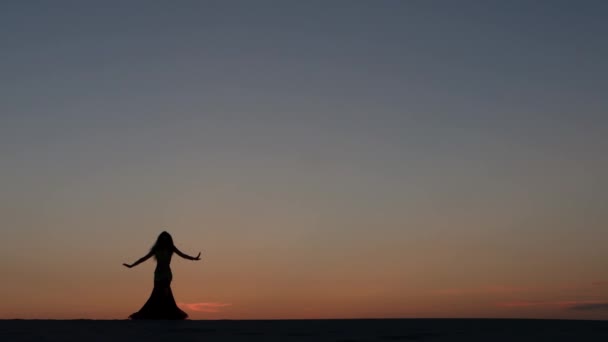 Chica bailando danza del vientre en la playa contra el atardecer. Siluetas — Vídeo de stock