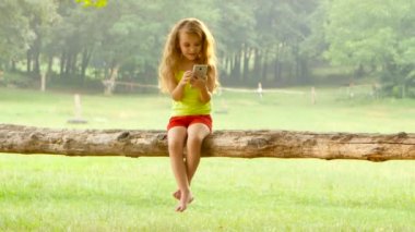 Bir ağaçta oturuyor smartphone oynamak sevimli küçük kız