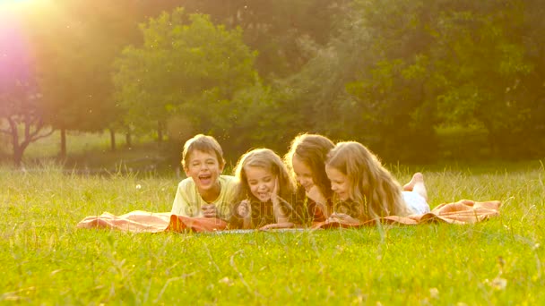 Niños felices hojean un libro en el jardín en el césped un día de verano — Vídeos de Stock