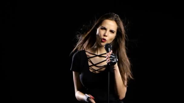 Mädchen in einem Mikrofon singt treibende Lieder und lächelt. schwarzer Hintergrund — Stockvideo