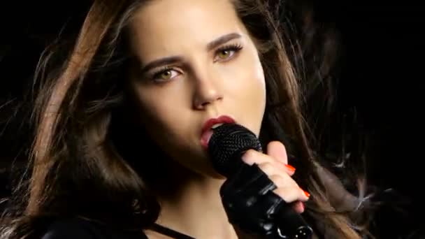 Girl in a microphone sings driving songs and smiles. Black background. Close up — Stock Video