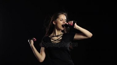 Kız bir mikrofon sürüş gülümser ve şarkı söylüyor. Siyah arka plan. Ağır çekim