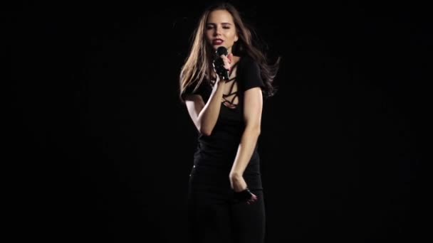 Die Sängerin hält einen Mikrofonständer in der Hand, ihre Haare entwickeln sich im Wind. schwarzer Hintergrund. Zeitlupe — Stockvideo