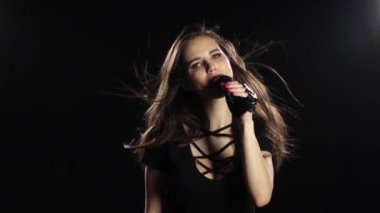 Kız bir mikrofon sürüş gülümser ve şarkı söylüyor. Siyah arka plan. Ağır çekim