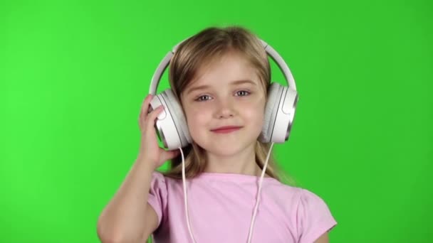 Baby luistert naar muziek via de hoofdtelefoon. Groen scherm. Slow motion — Stockvideo