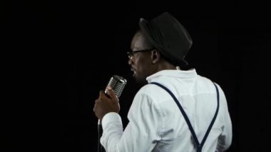 Adam şarkıcı arka görünümünden bir mikrofon ve dans içine şarkı söylüyor. Siyah arka plan. Yakın çekim