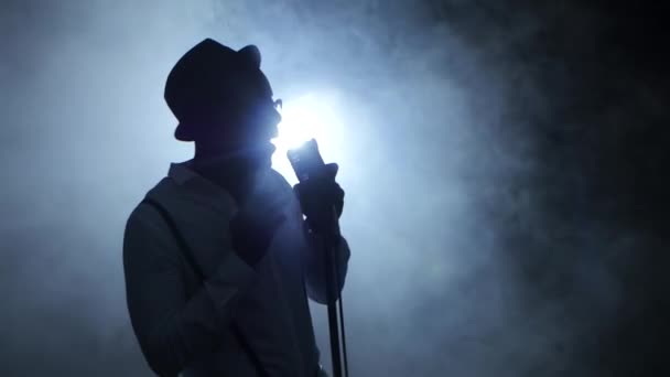 Músico afroamericano en el humo y la luz blanca cantando en un estudio de grabación. Fondo negro. Silueta — Vídeo de stock
