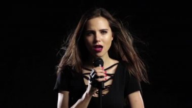 Kız mikrofon hassas şarkıları shes karizmatik söylüyor. Siyah arka plan. Ağır çekim