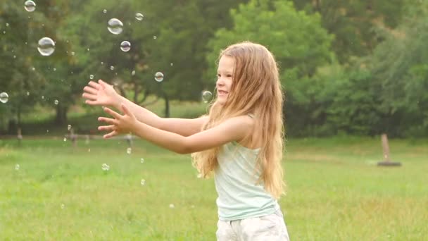 Ragazza allegra gioca prendere bolle di sapone sul prato. Al rallentatore. Da vicino. — Video Stock