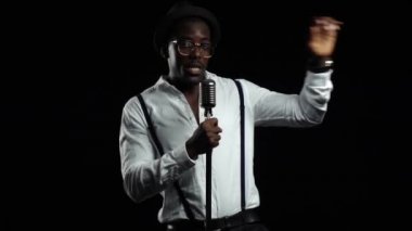 Şarkıcı bir mikrofona iplik atlama ve onun etrafında dans şarkı söylüyor. Siyah arka plan. Ağır çekim. Yakın çekim