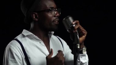 Adam şarkıcı şarkı söylüyor bir mikrofon ve dans içine. Siyah arka plan. Ağır çekim. Yakın çekim