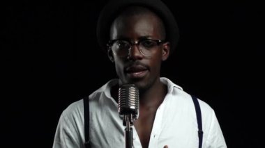 Retro bir mikrofon ve yanında dans içine gesticulating şarkıcı söylüyor. Siyah arka plan. Ağır çekim. Yakın çekim