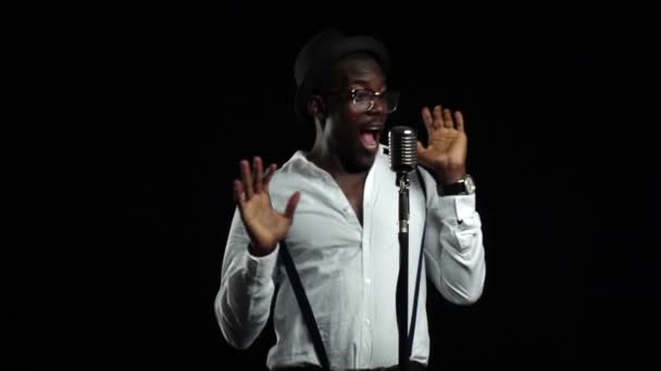 Un uomo afroamericano canta in un microfono e balla. Fondo nero. Al rallentatore. Da vicino. — Video Stock