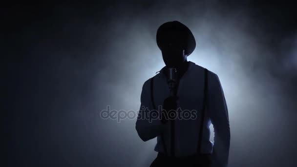 Hudebník v kouři v bílé světlo zpěv na mikrofon. Černé pozadí. Silueta. Zpomalený pohyb — Stock video
