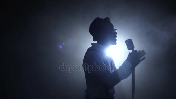 Cantante la mitad de la facturación en el humo y la luz blanca cantando en el micrófono. Fondo negro. Silueta. Movimiento lento — Vídeos de Stock