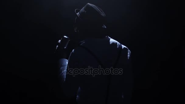 Singer in the dark with a weak light at the microphone singing the song. Black background. Silhouette. Slow motion. Close up — Stock Video