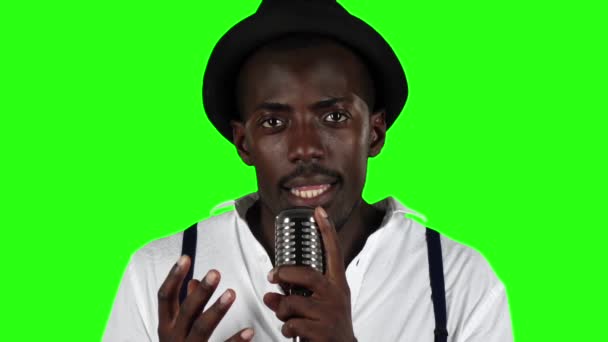 Killen med mustasch och skägg bär en hatt och solglasögon sjunger i en retro mikrofon. Grön skärm. Slow motion. Närbild — Stockvideo