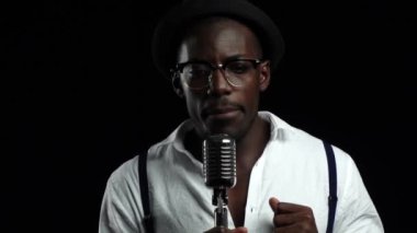 Adam genç Afro-Amerikan şarkı bir mikrofona bir kayıt stüdyosu. Siyah arka plan. Ağır çekim. Yakın çekim