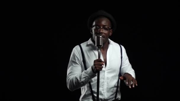 Afro-américain avec des lunettes chantant et dansant sur la musique du microphone. Fond noir. Au ralenti. Gros plan — Video