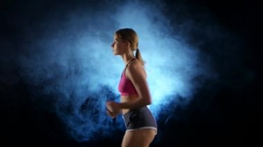 Sahne ışıkları altında duman tarafından aydınlatılmış siyah bir arka plan üzerinde çalışan kız. Yakın çekim