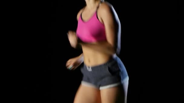 Chica deportiva en pantalones cortos con bolsillos que corren sobre un fondo negro. De cerca. — Vídeos de Stock