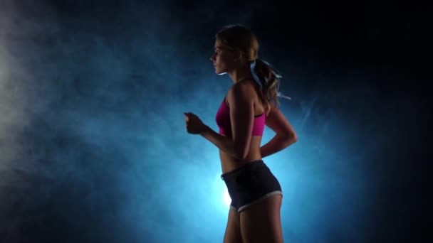Θέα από το πλάι στο τρέξιμο κορίτσι σε ένα καπνιστή μαύρο προσκήνιο φόντο. Αργή κίνηση — Αρχείο Βίντεο