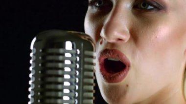 Kız retro bir mikrofon şarkı söylüyor. Siyah arka plan. Yan görünümü. Yakın çekim