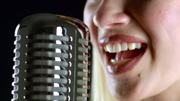 Cantante canta en un micrófono retro. Fondo negro. Vista lateral. De cerca. — Vídeo de stock