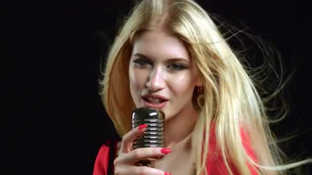 A rapariga canta num microfone retrô, com o cabelo a tremer ao vento. Fundo preto. Vista lateral — Vídeo de Stock