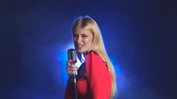 Menina em um vestido vermelho está cantando em um microfone retro. Fundo de fumo — Vídeo de Stock