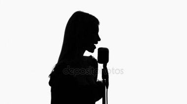 Seksi ve nazik sings bir retro mikrofon müzik sanatçısıdır. Siluet. Yan görünümü. Beyaz arka plan