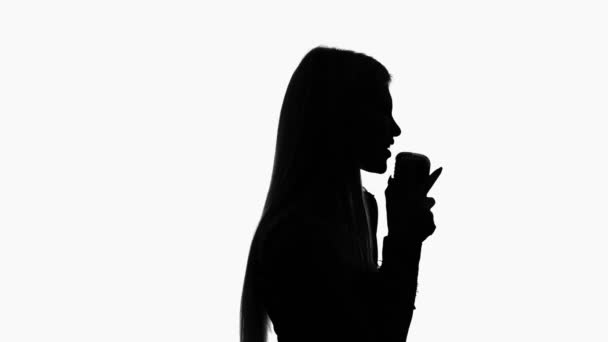 Vocalist in a dress is singing into a retro microphone. Silhouette. Side view. White background — Stock Video