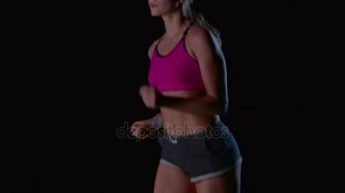 Sportif cepli siyah bir arka plan üzerinde çalışan şortlu kız. Ağır çekim. Yakın çekim