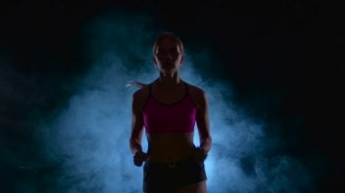 Kız fitness sürekli çalışır. Önden Görünüm. Duman siyah ekran. Siluet. Ağır çekim. Yakın çekim