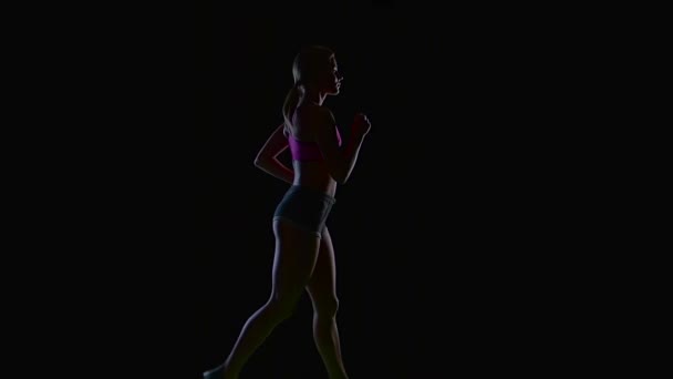 Sportlerin läuft wunderschön in einer halben Drehung auf schwarzem Hintergrund. Silhouette. Zeitlupe — Stockvideo