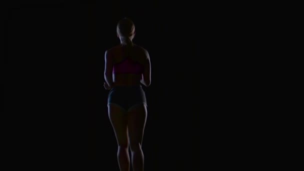 Atlética mujer fitness corriendo vista trasera sobre un fondo negro. Silueta. Movimiento lento — Vídeos de Stock