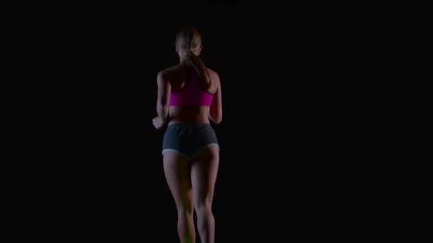 Frau joggt rückwärts auf schwarzem Hintergrund. Silhouette. Zeitlupe — Stockvideo
