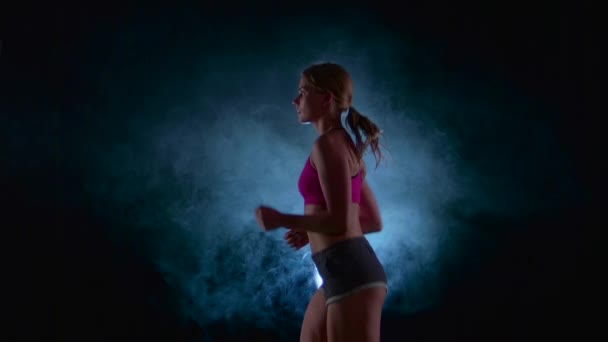 Κορίτσι να τρέχει πάνω σε μαύρο φόντο που φωτίζεται από τα φώτα της δημοσιότητας στον καπνό. Αργή κίνηση. Κοντινό πλάνο — Αρχείο Βίντεο