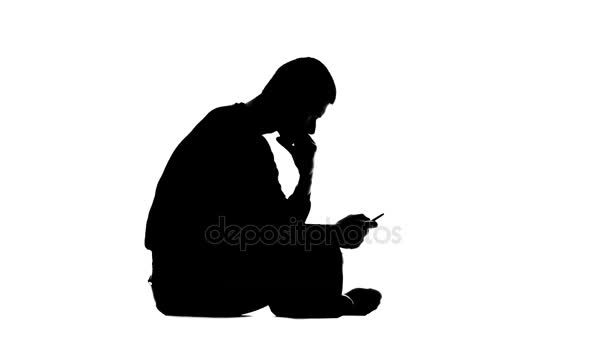 Ο τύπος κρατώντας το τηλέφωνο και κάθεται στο πάτωμα. Λευκό φόντο. Σιλουέτα — Αρχείο Βίντεο