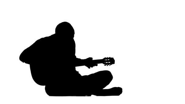 Muzikant speelt gitaar zittend op de vloer. Silhouet. Witte achtergrond — Stockvideo