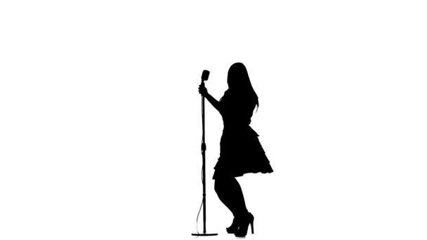 Mulher canta música e dança perto de um microfone retro. Silhueta. Fundo branco — Vídeo de Stock