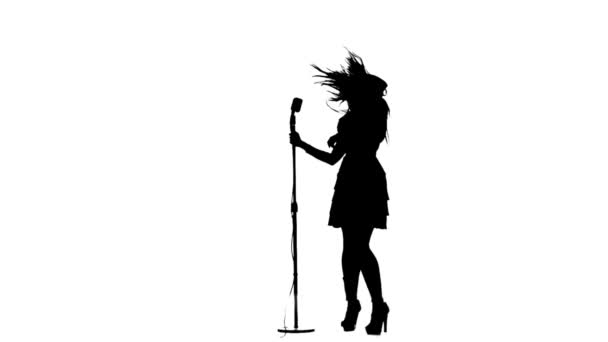 Une femme chante et danse près d'un microphone rétro. Silhouette. Fond blanc. Mouvement lent — Video