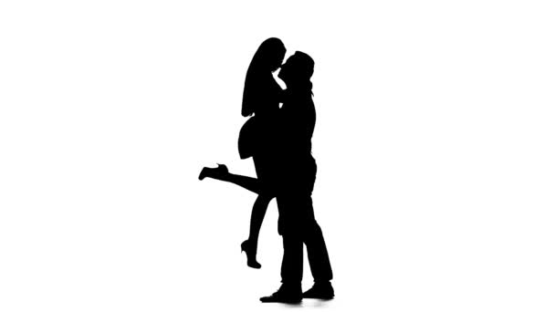 Killen tar flickan i sina armar och kyssar. Siluett. Vit bakgrund. Slow motion — Stockvideo